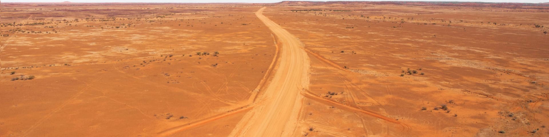 A vast, arid landscape with a winding dirt road cutting through it.