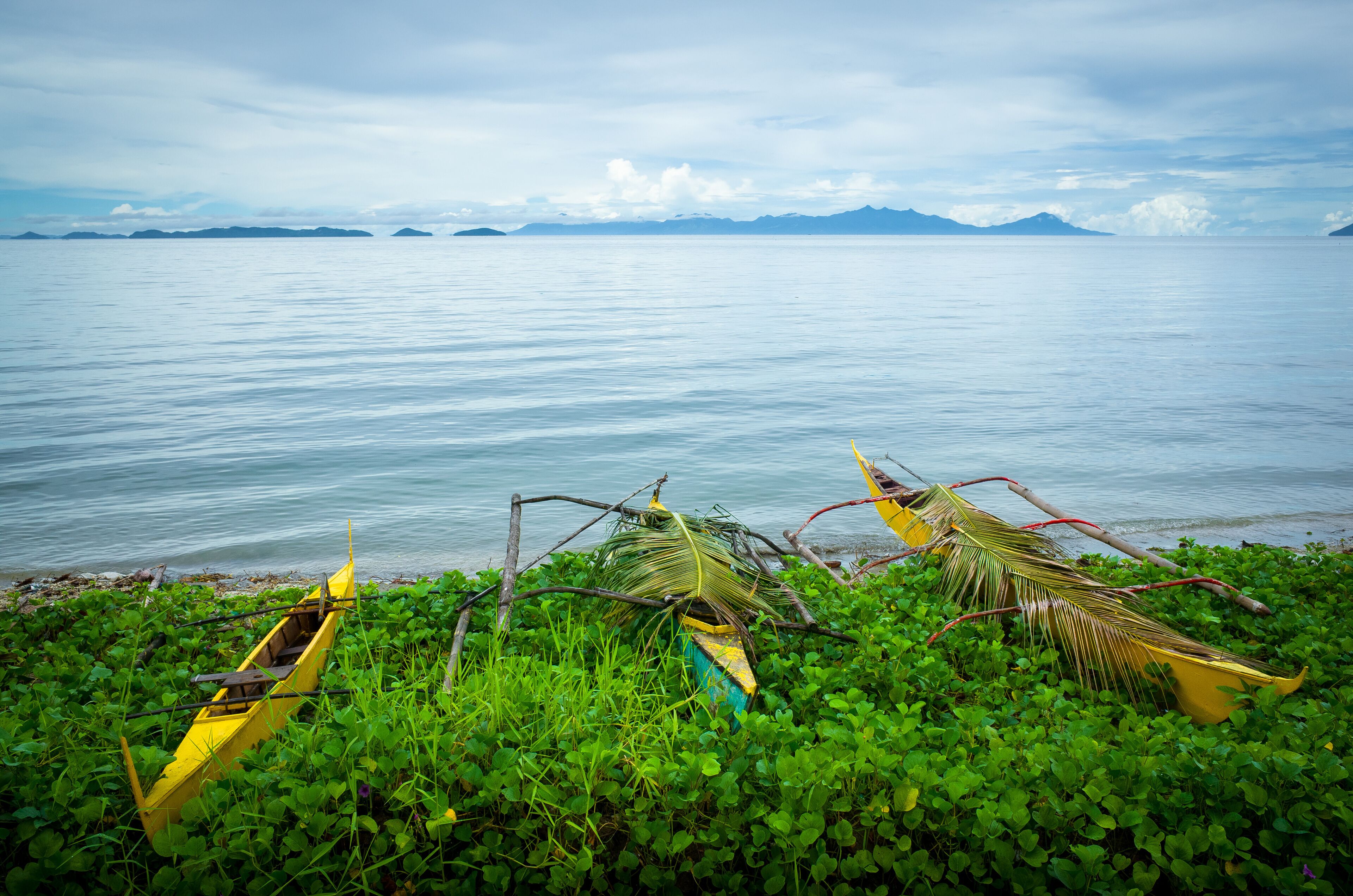 A calm sea with a yellow boat and a hammock on a grassy shore.