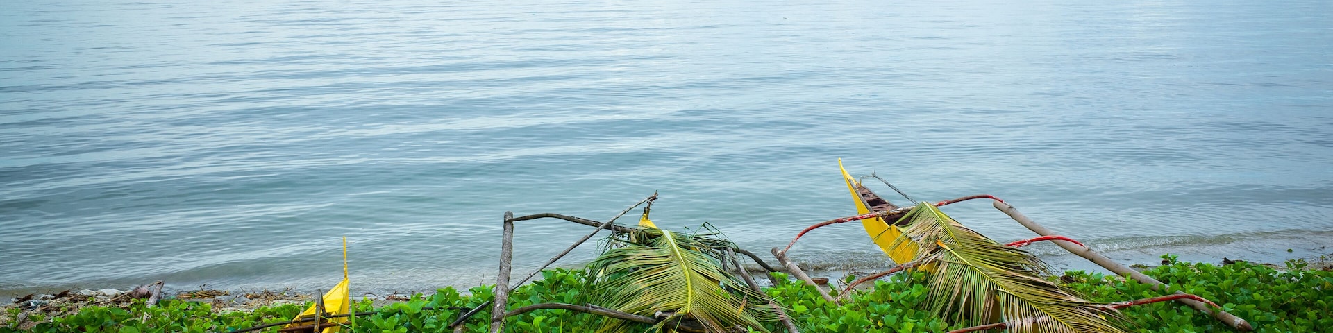 A calm sea with a yellow boat and a hammock on a grassy shore.