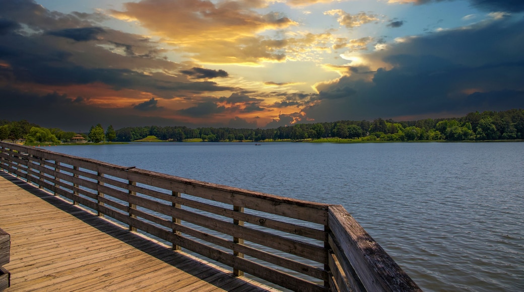 a brown wooden bridge over the silky green waters of Lake Acworth surrounded by lush green trees and plants with powerful clouds at sunset at Cauble Park in Acworth Georgia USA