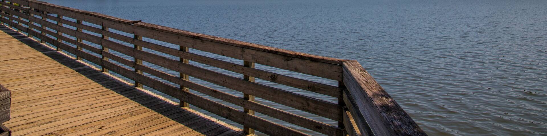 a brown wooden bridge over the silky green waters of Lake Acworth surrounded by lush green trees and plants with powerful clouds at sunset at Cauble Park in Acworth Georgia USA