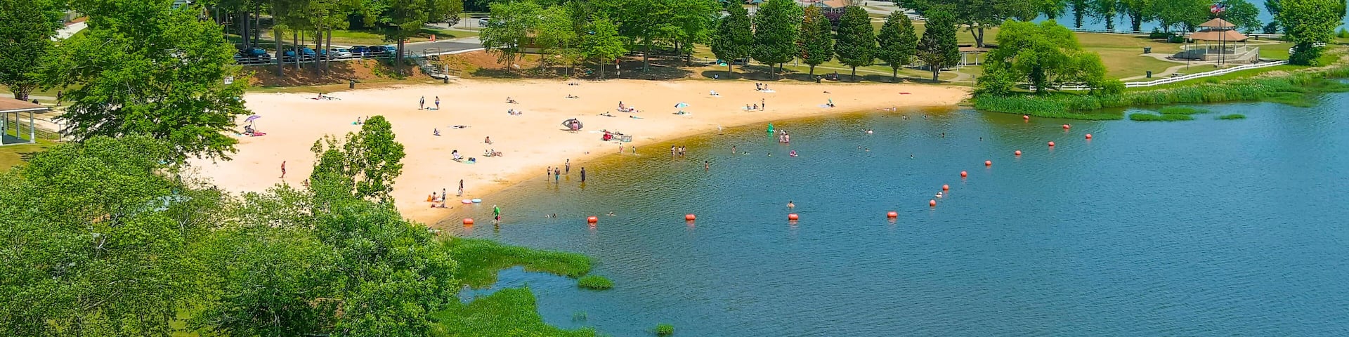 an aerial shot of people relaxing on the beach at Lake Acworth with silky brown sand and blue lake water surrounded by lush green trees and grass with blue sky at Cauble Park in in Acworth Georgia USA