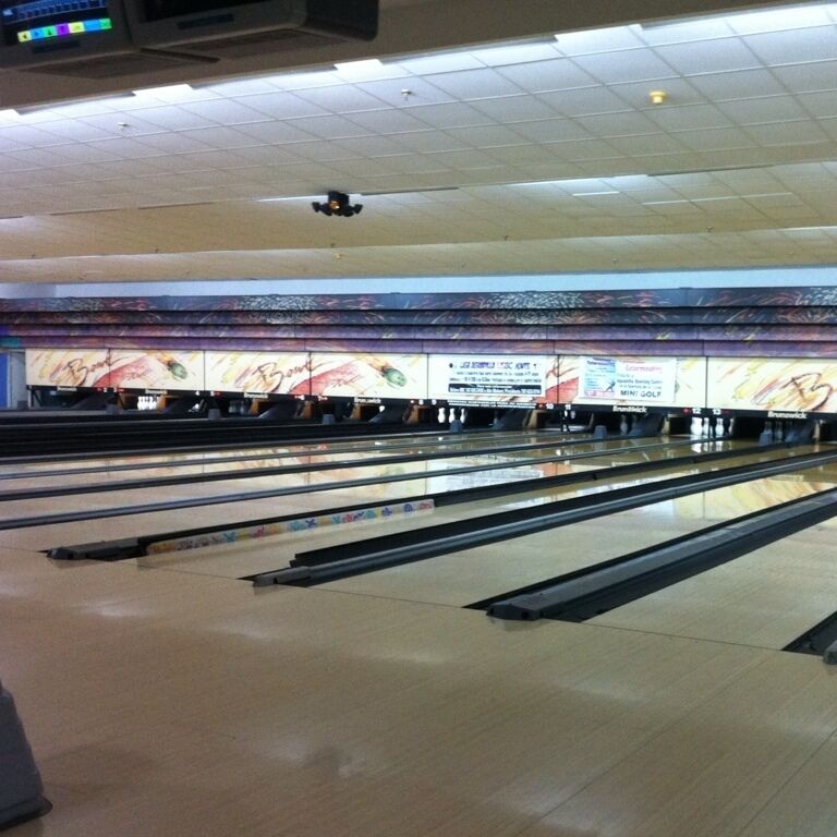 A bowling alley with multiple lanes and a colorful mural on the back wall.