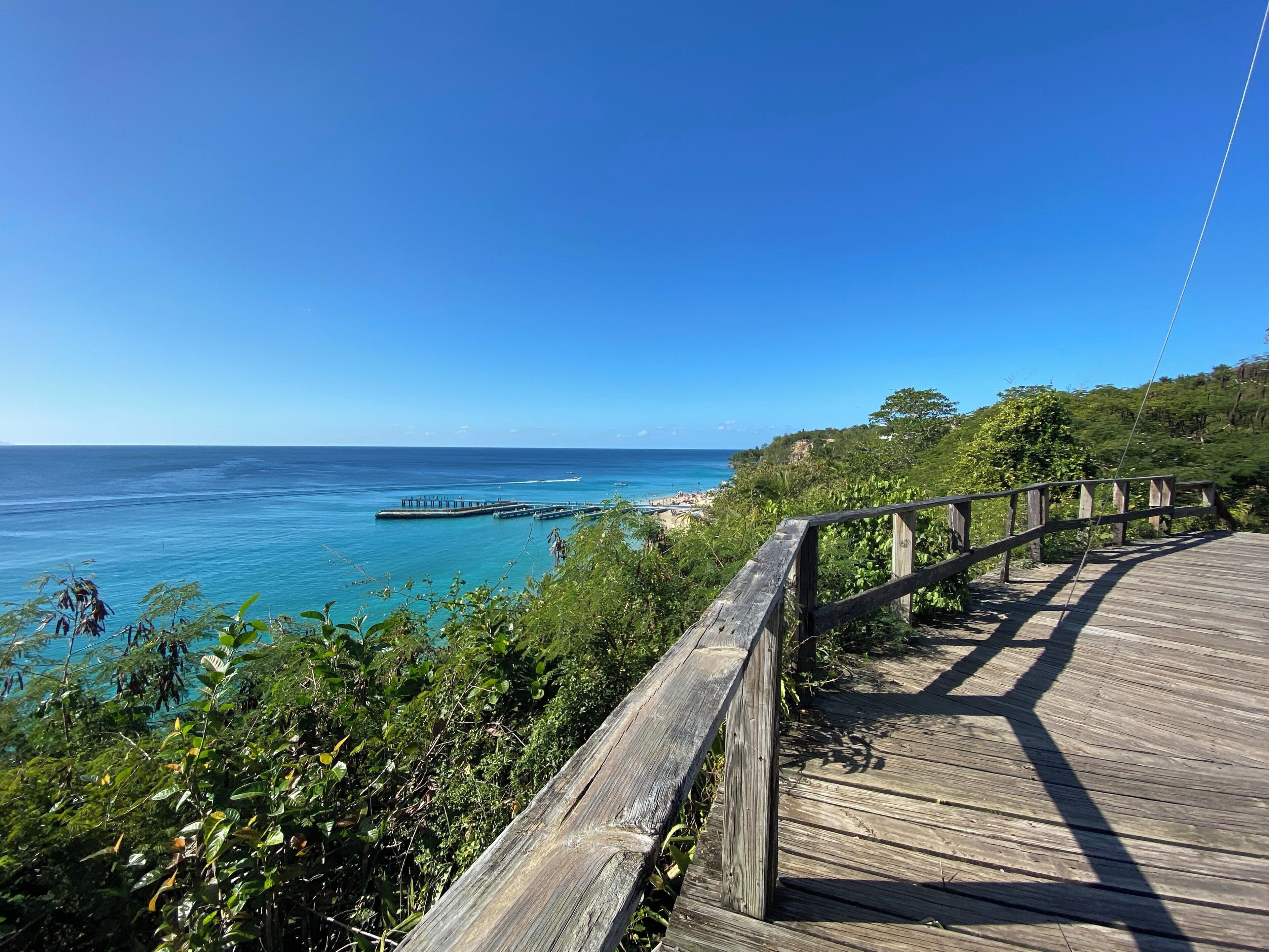 A wooden boardwalk overlooking a beach with a pier extending into the ocean.