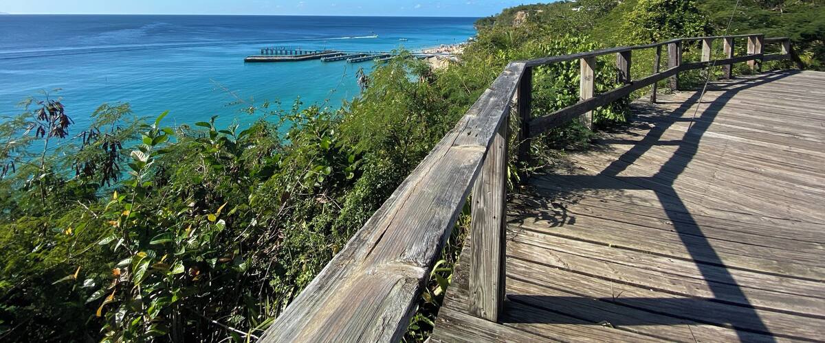 A wooden boardwalk overlooking a beach with a pier extending into the ocean.