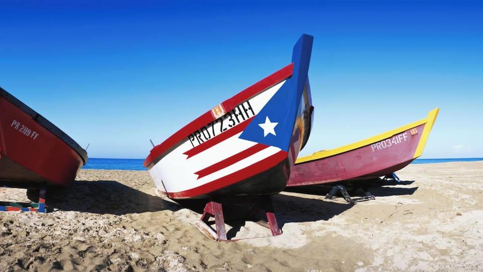 Three boats on a sandy beach with a clear blue sky.