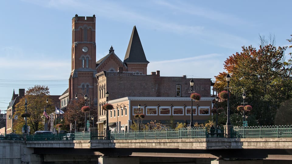 A historic church with a tall tower and a steeple, a bridge with a green fence, and autumn trees with red leaves.