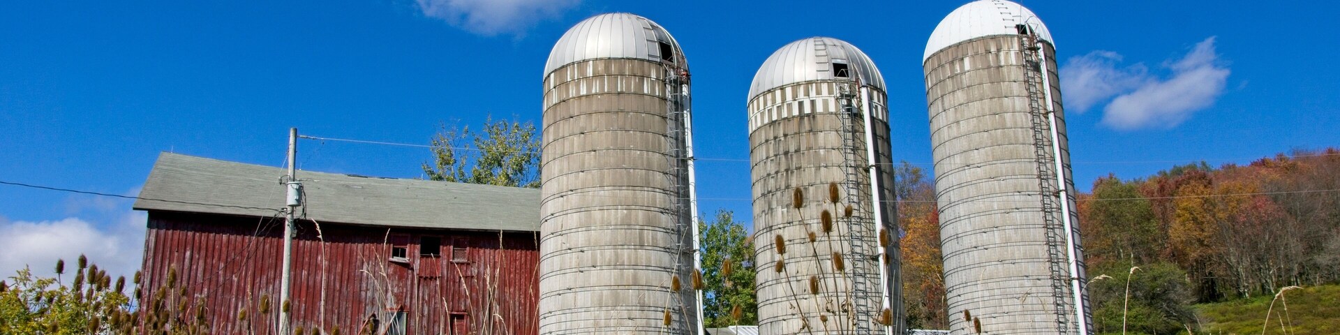 Tres silos, un granero rojo y un cielo azul despejado con nubes.