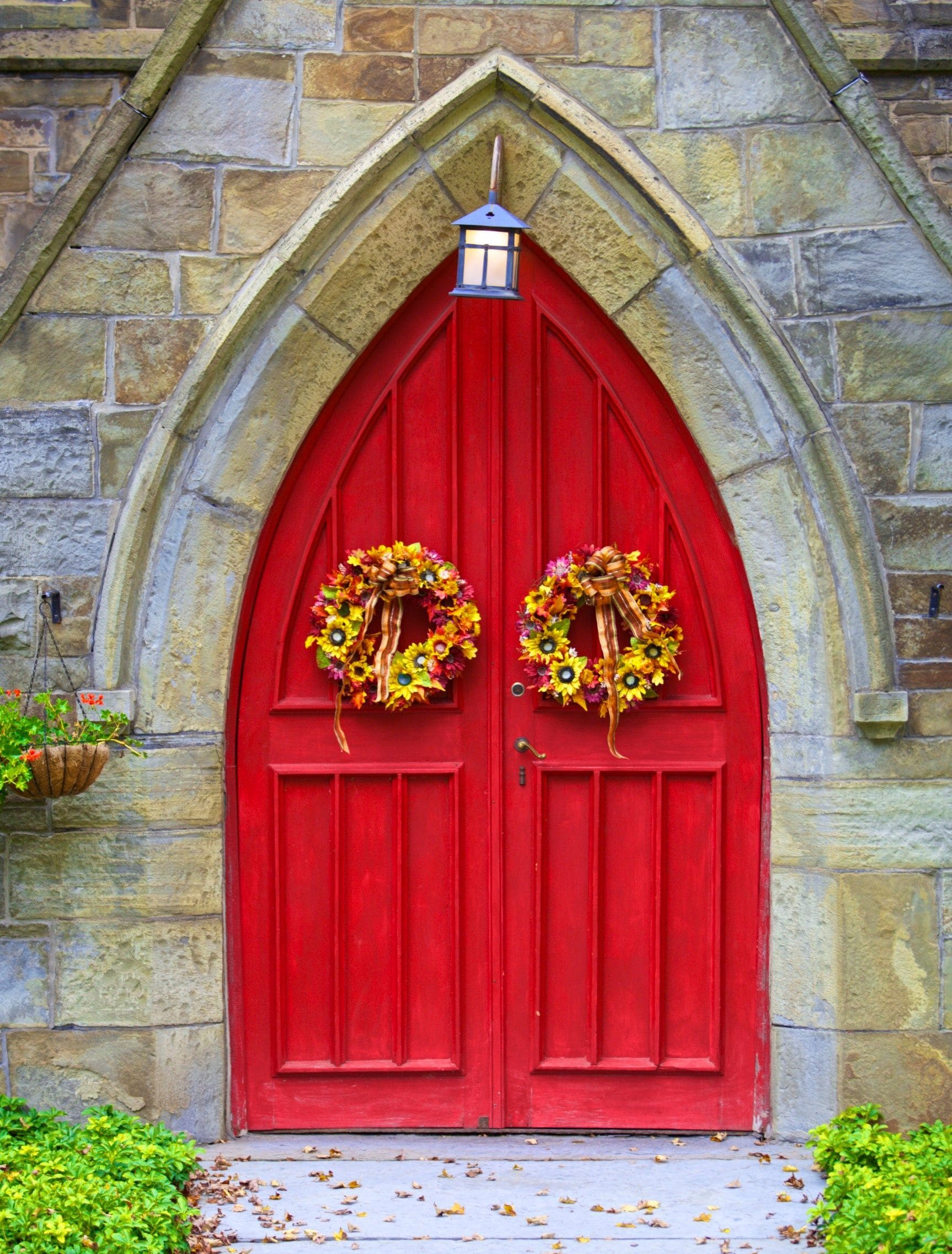 A red church door with two floral wreaths.