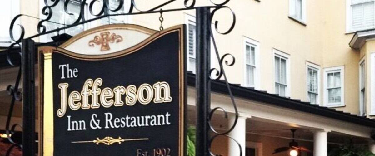 A sign for The Jefferson Inn & Restaurant with a patio area and plants in front.