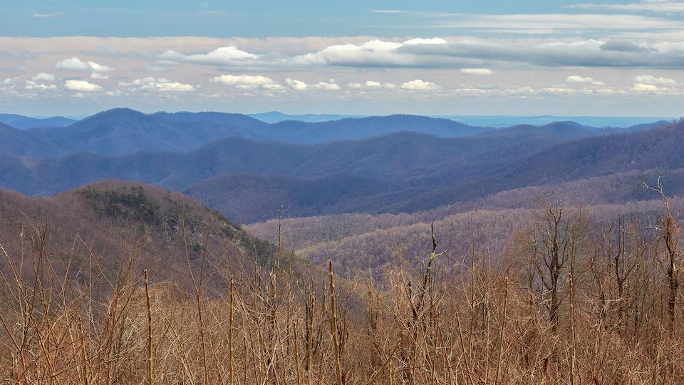 A mountainous landscape with a valley and distant hills under a partly cloudy sky.