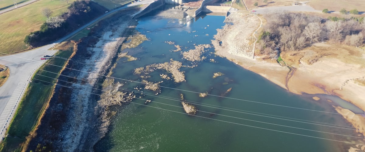 A dam with a water reservoir, a road, and a distant building.