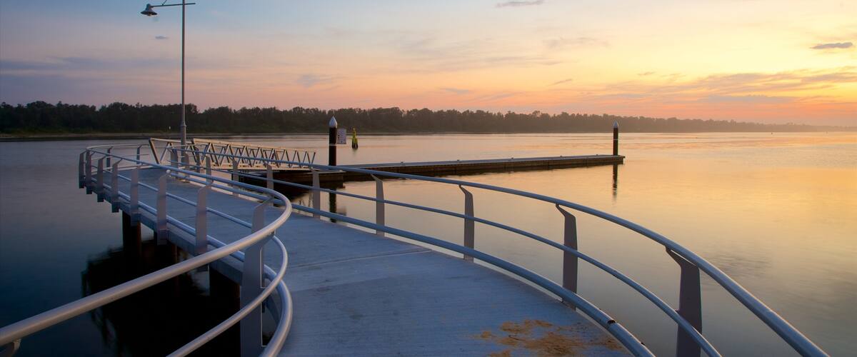 A pier extending into calm water with a sunset in the background.