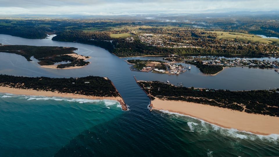An aerial view of a coastal area with a beach, a river, and a town.