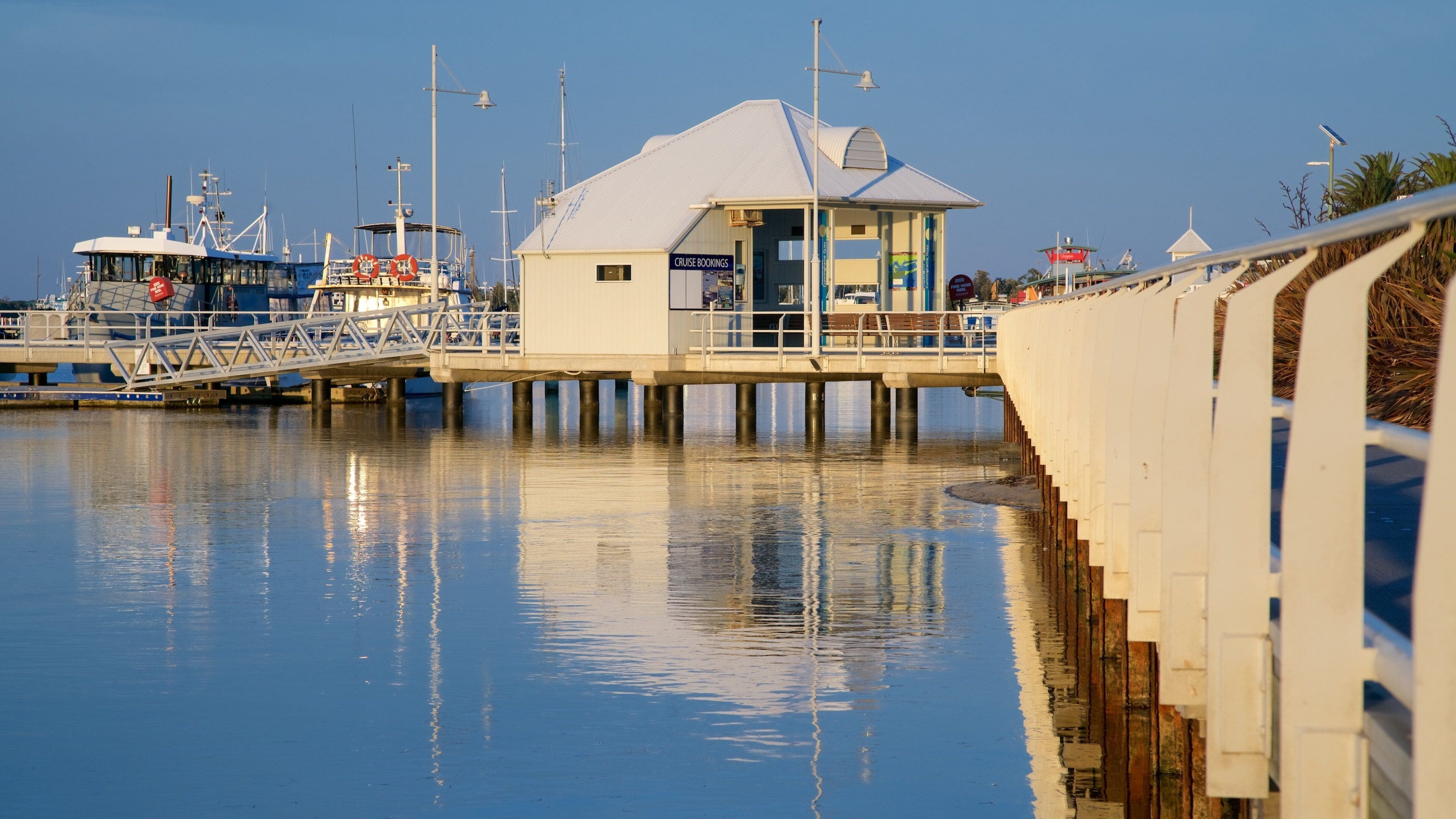 A pier with a lifebuoy, a boat, and a building with a 'Cruise Bookings' sign.