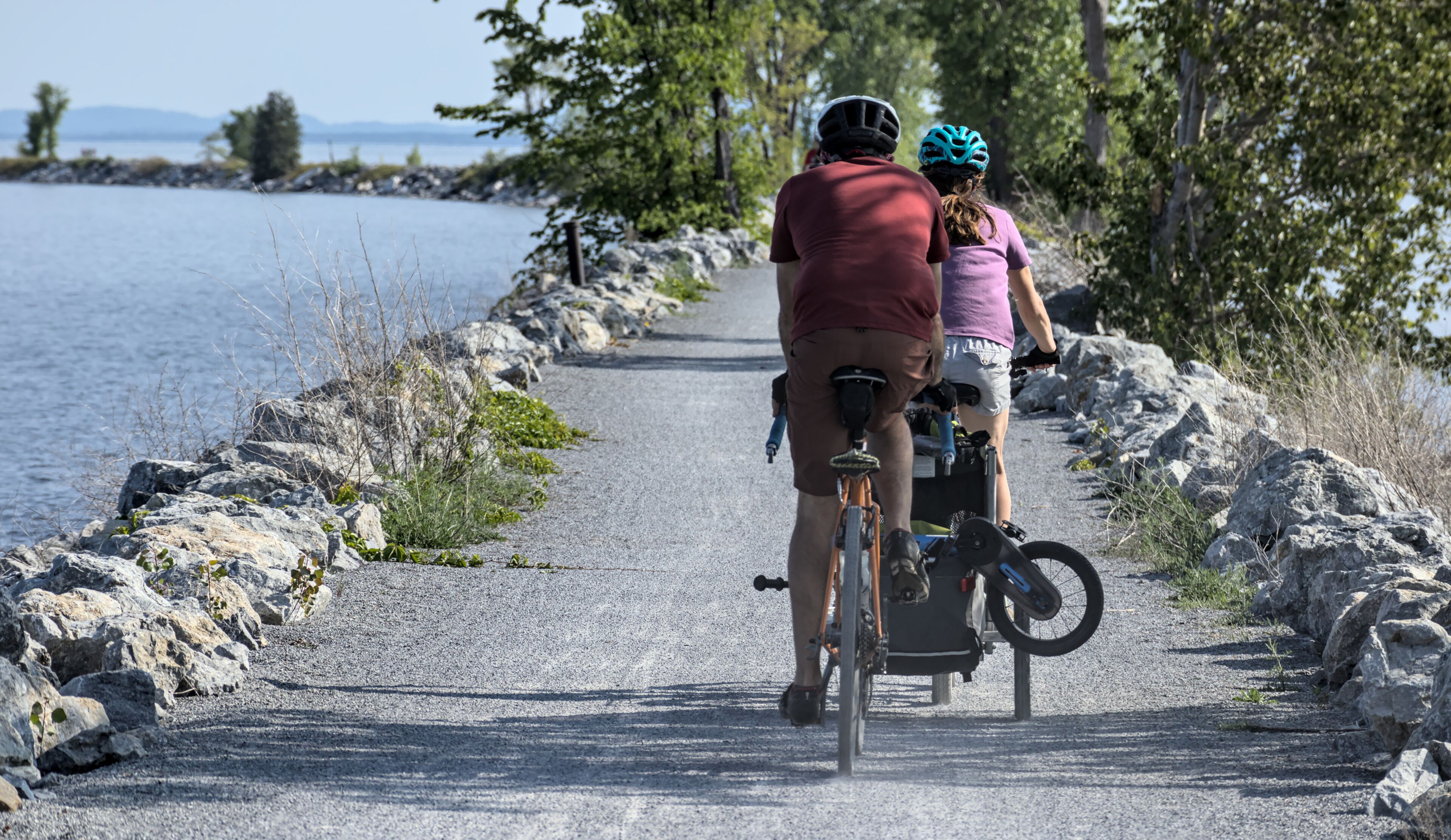 people riding a bike on the colchester causeway gravel bike path in burlington, vermont (mountain bikes with kid's bike) from behind, unrecognizable (sport, recreation, travel, bike riding, cycling)