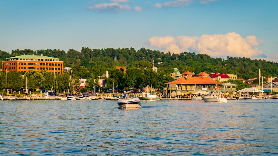 A waterfront with boats, a red building, and a hill with trees.