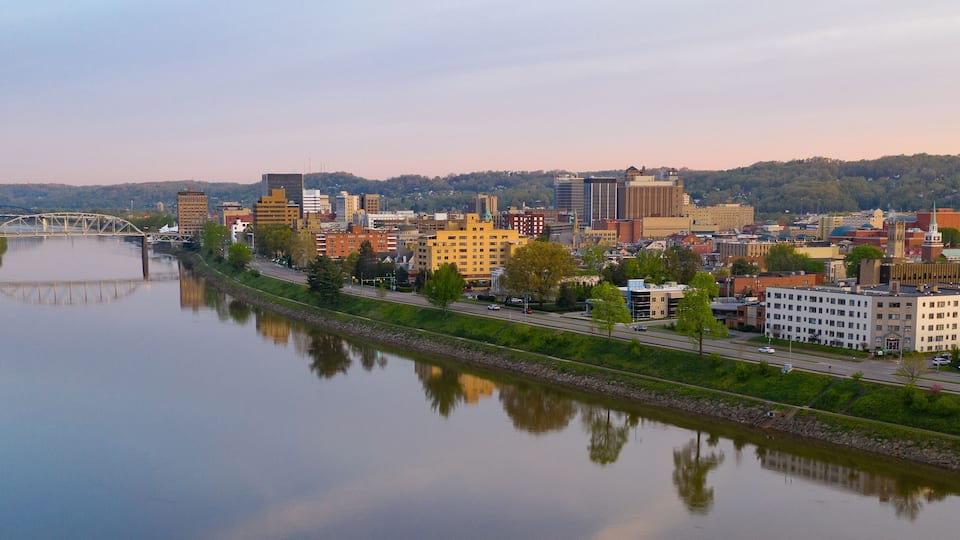 A river with a bridge, a cityscape with various buildings, and a hilly background.