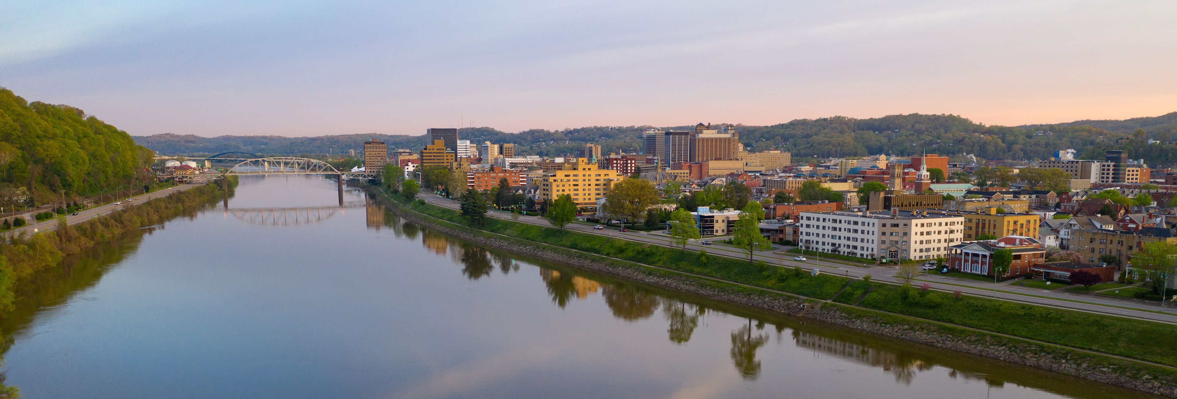 A river with a bridge, a cityscape with various buildings, and a hilly background.