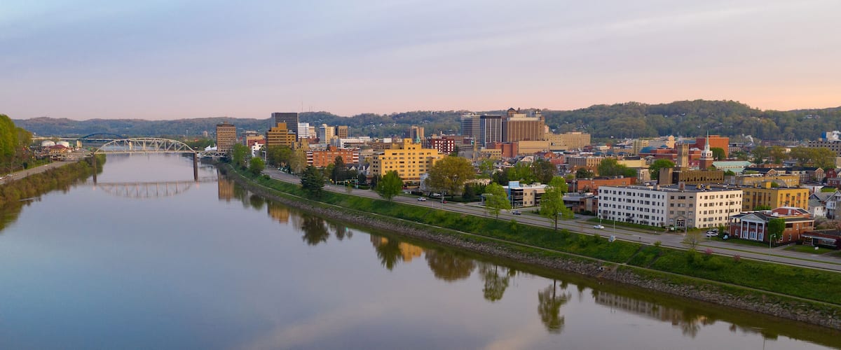 A river with a bridge, a cityscape with various buildings, and a hilly background.