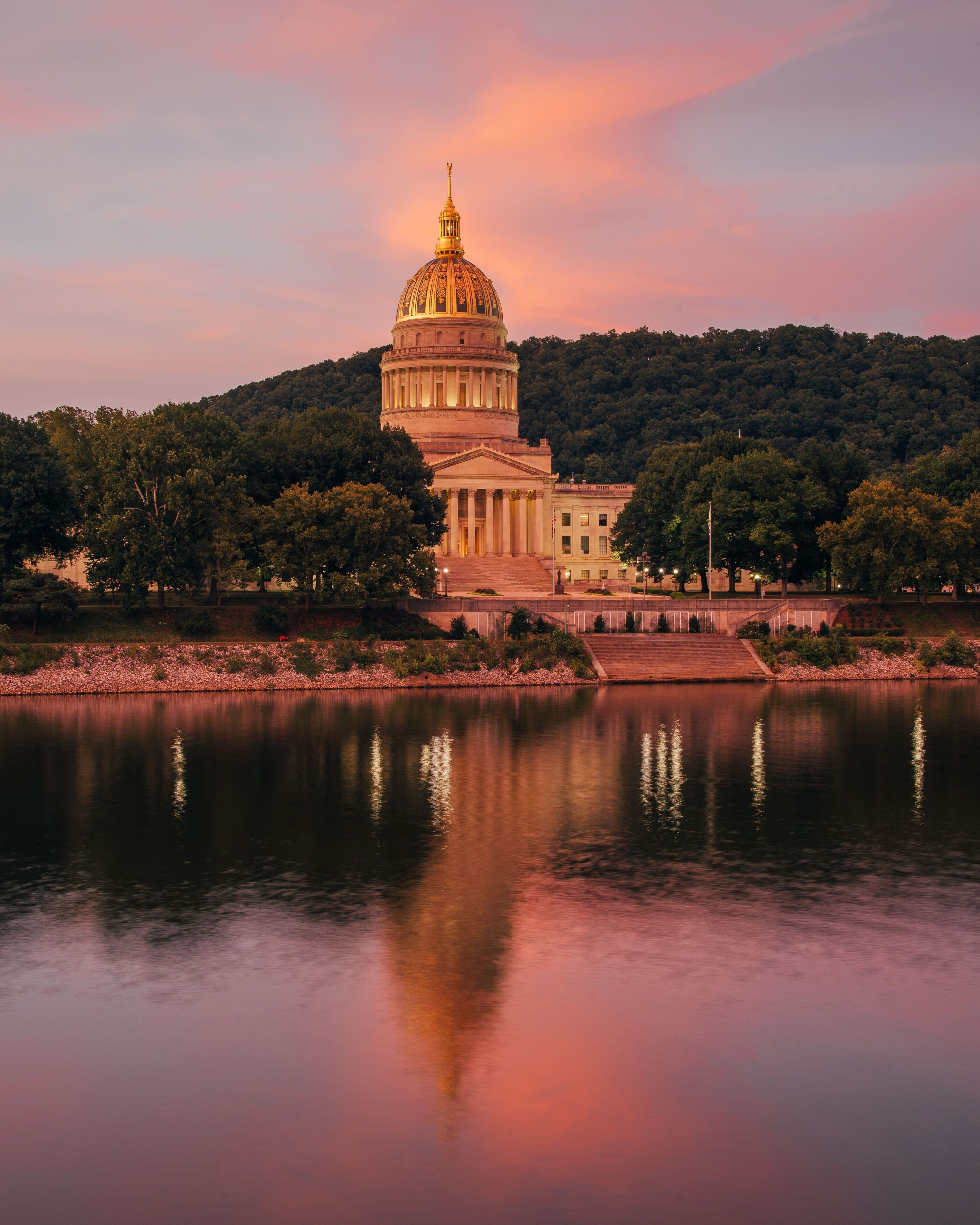 A large domed building with a reflection in the water, surrounded by trees and hills.