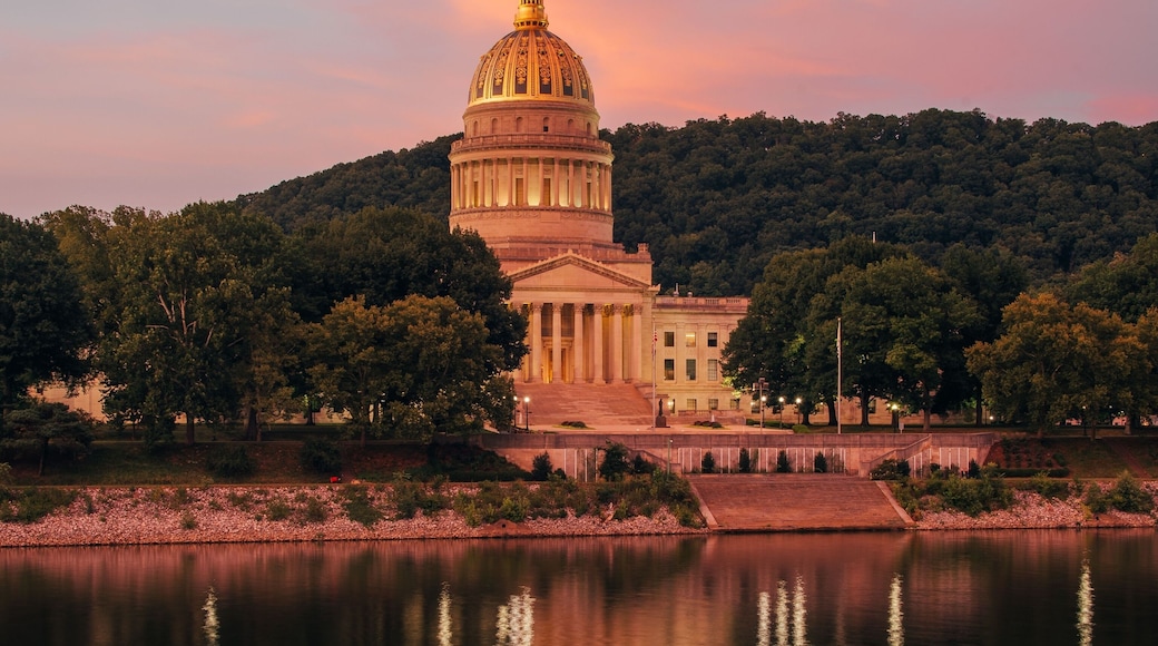 A large domed building with a reflection in the water, surrounded by trees and hills.