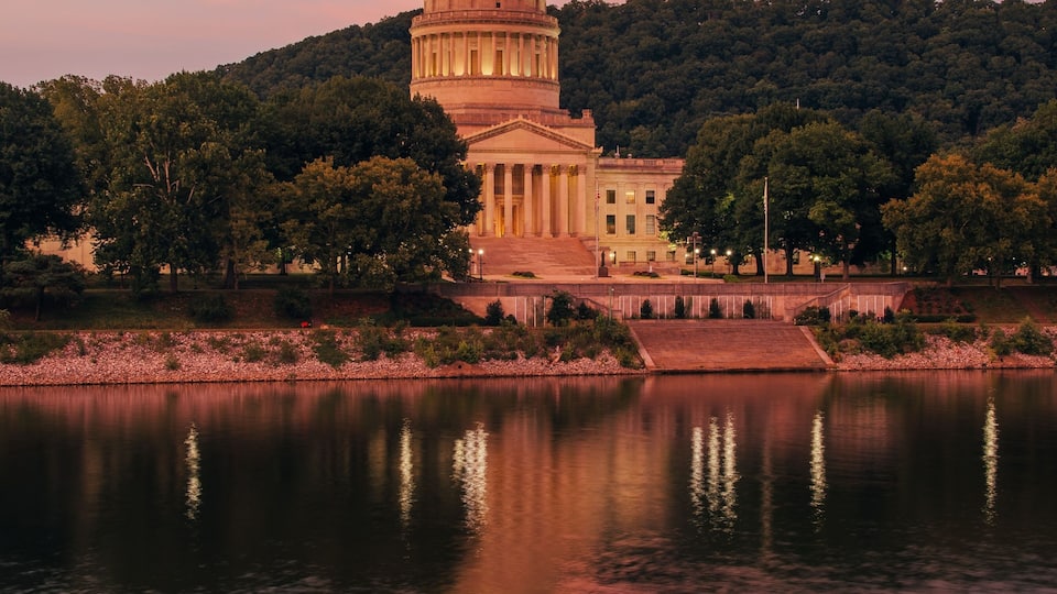 A large domed building with a reflection in the water, surrounded by trees and hills.
