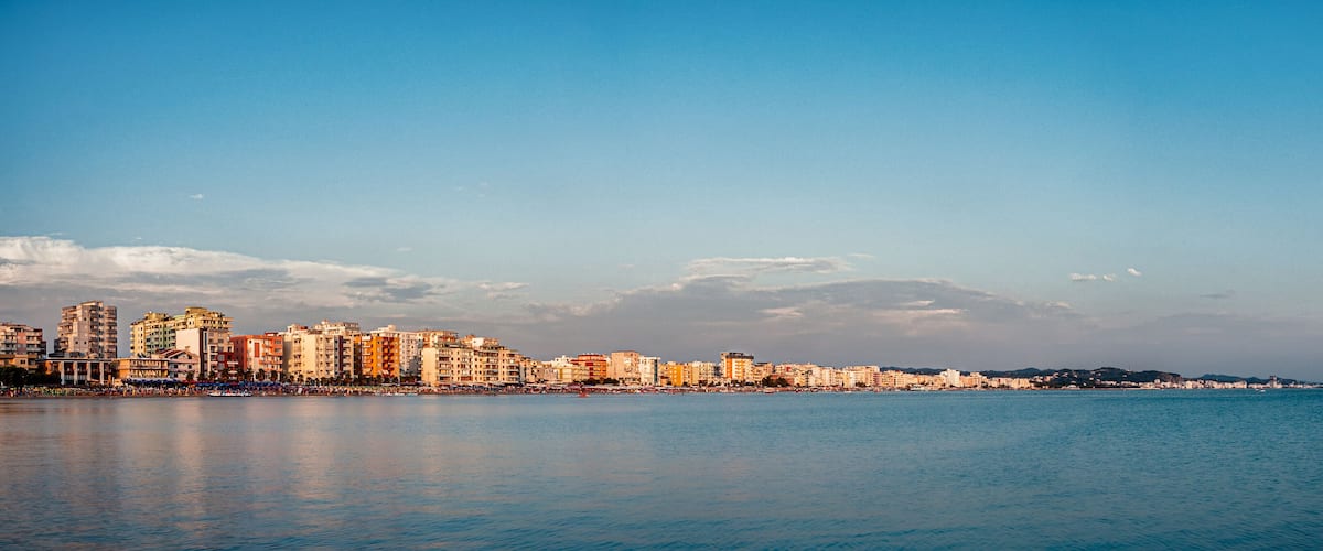 A coastal cityscape with a clear sky, calm sea, and a variety of buildings along the waterfront.