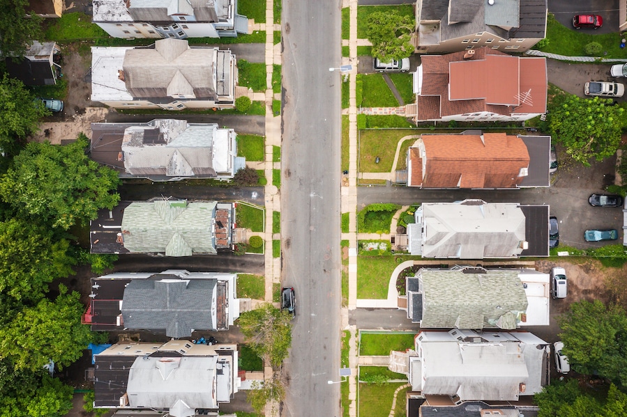 An aerial view of a residential street with houses, cars, and green lawns.