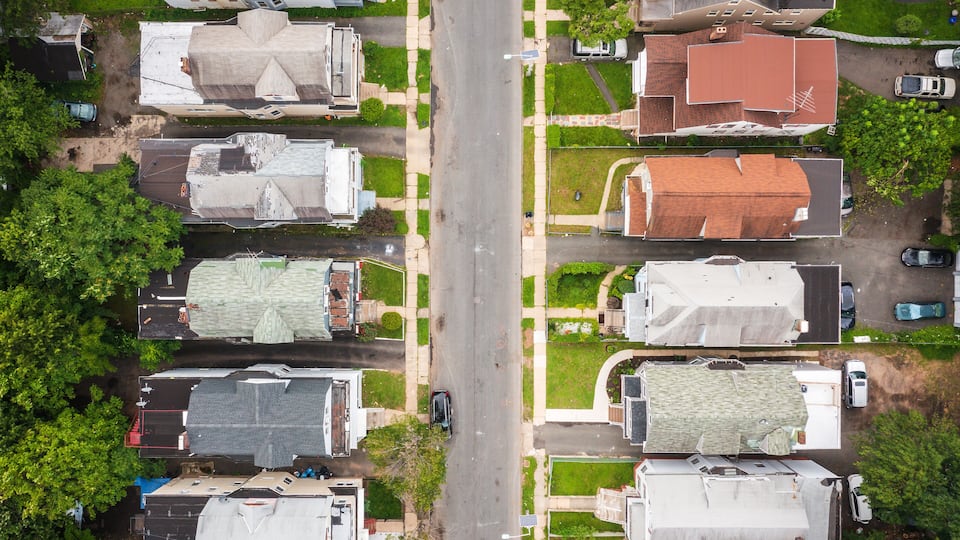 An aerial view of a residential street with houses, cars, and green lawns.