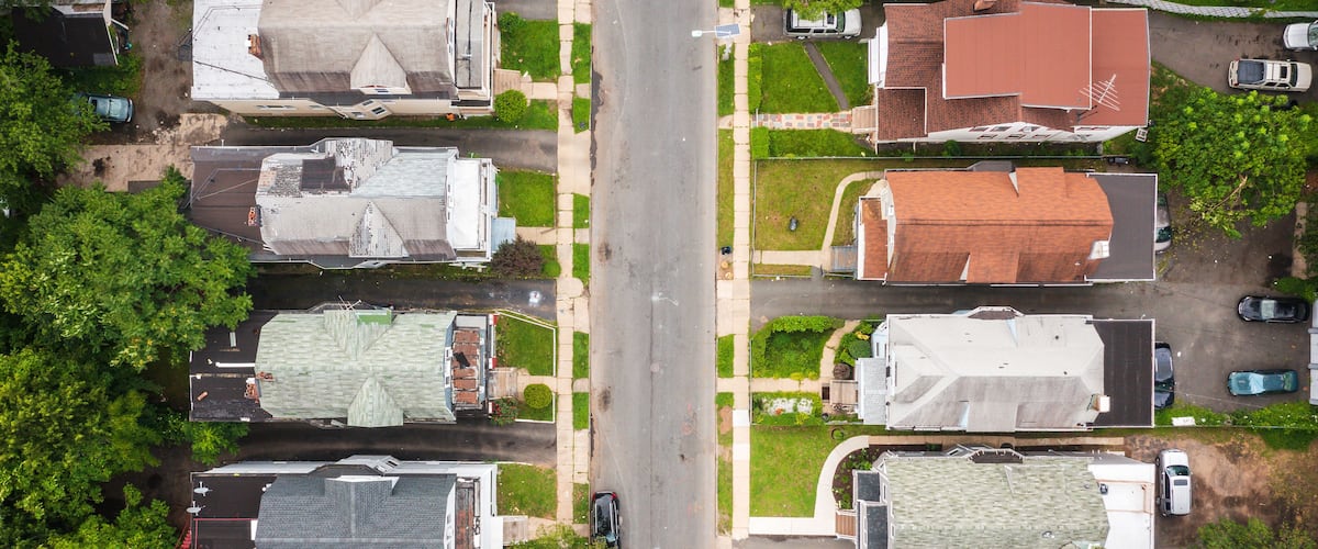 An aerial view of a residential street with houses, cars, and green lawns.