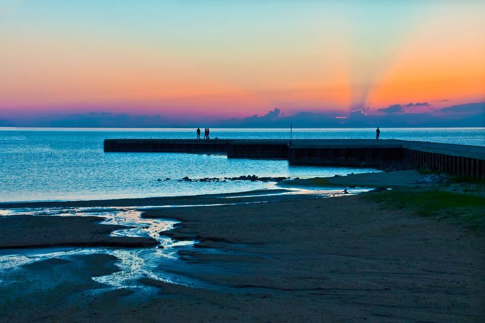 A sunset over a beach with a pier and people walking.