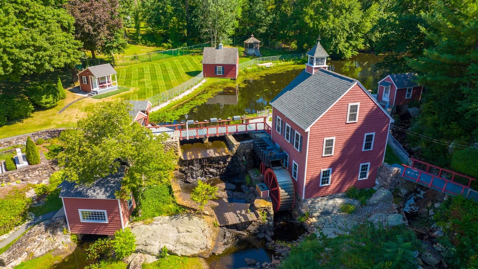 A historic watermill with a red brick building, a small house, and a pond.