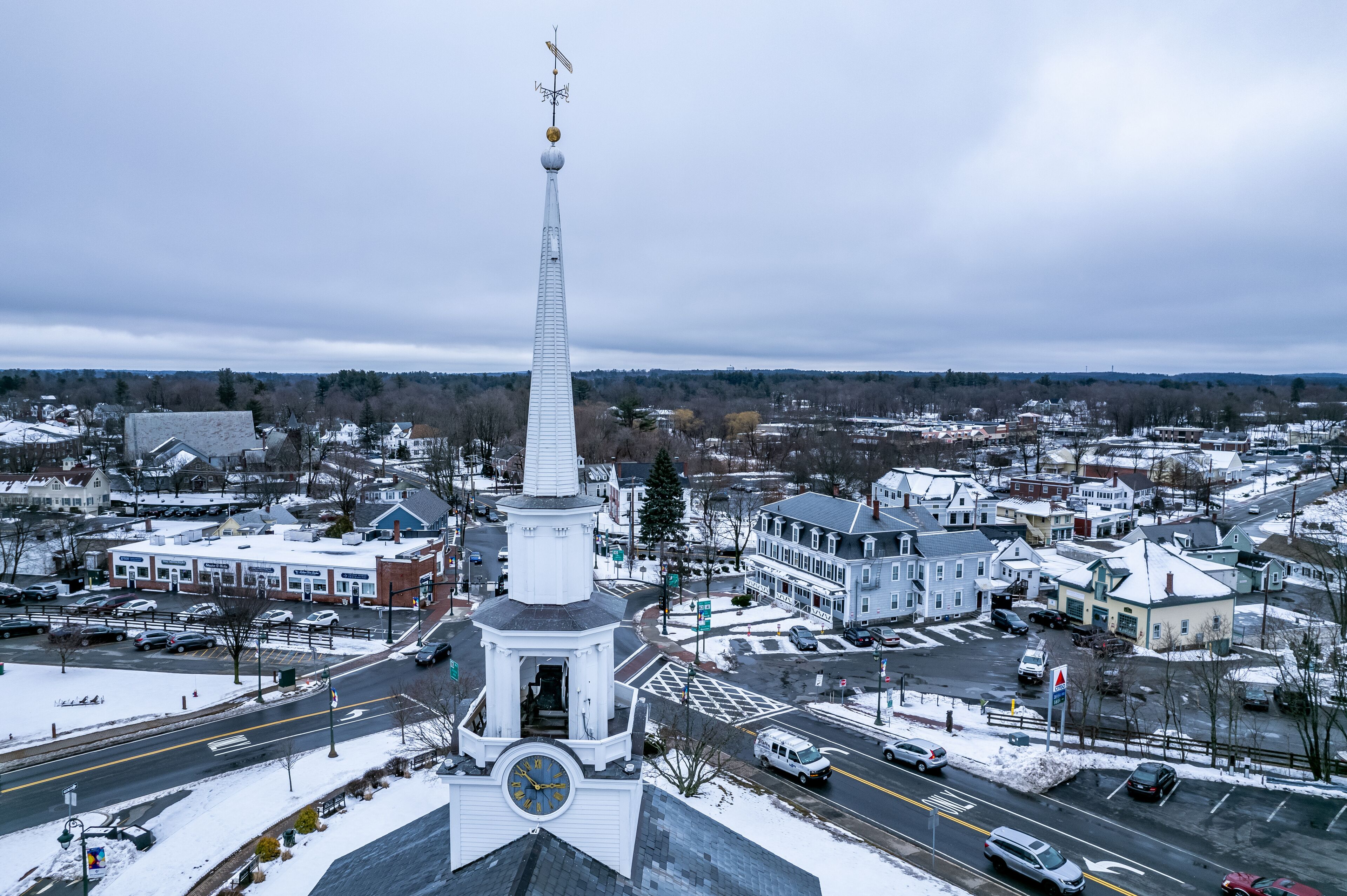 A town with a prominent white church steeple, a snow-covered landscape, and a mix of residential and commercial buildings.