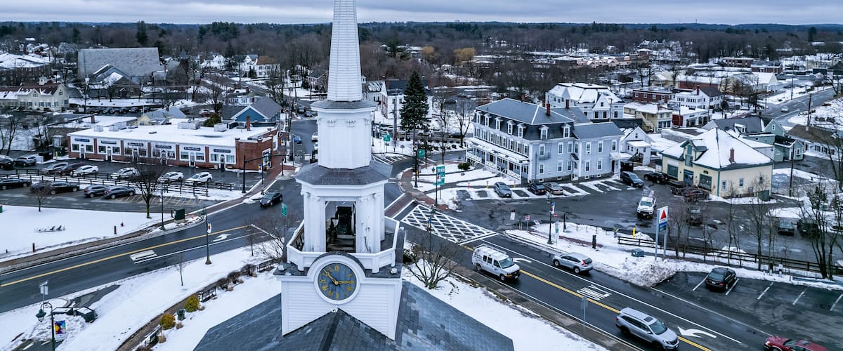 A town with a prominent white church steeple, a snow-covered landscape, and a mix of residential and commercial buildings.