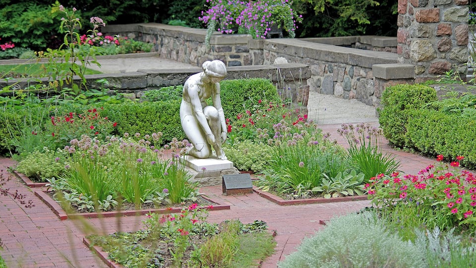 A garden with a statue, various plants, and a stone wall.