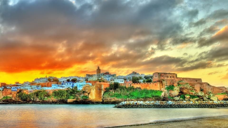 A coastal cityscape with a prominent fort and buildings against a sunset sky.