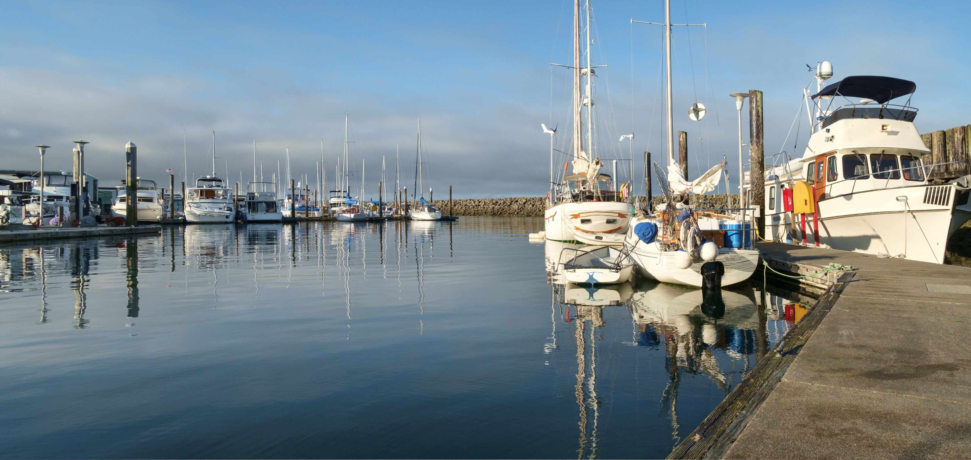 A marina with various boats docked, calm water, and a wooden pier.