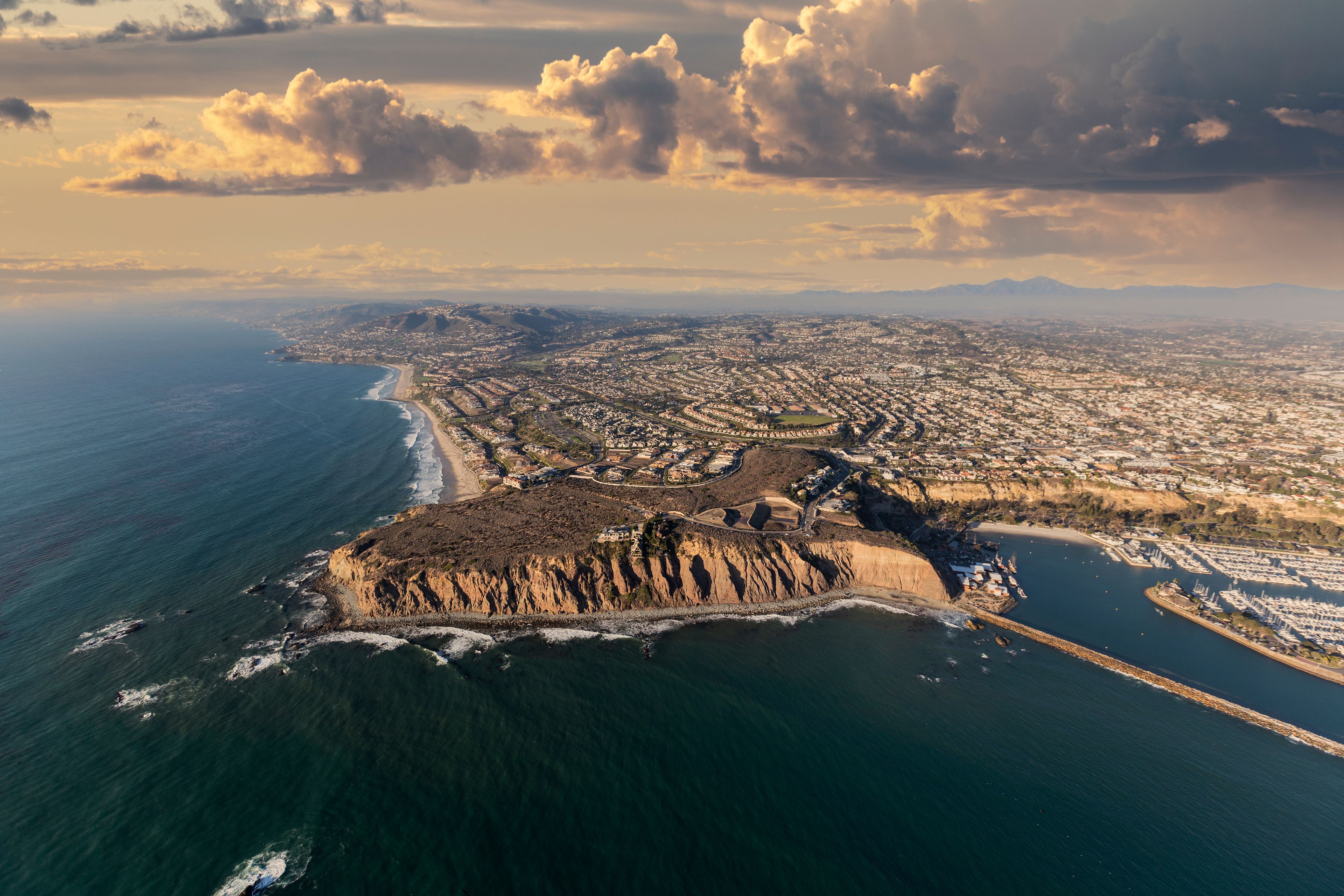 An aerial view of a coastal city with a prominent cliff, a marina, and a beach.