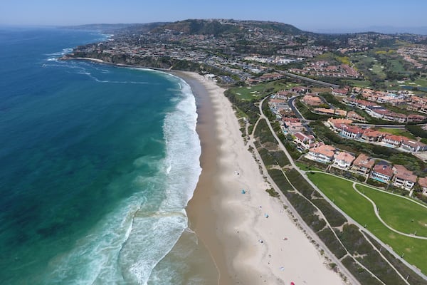 A coastal town with a beach, houses, and a hilly landscape in the background.