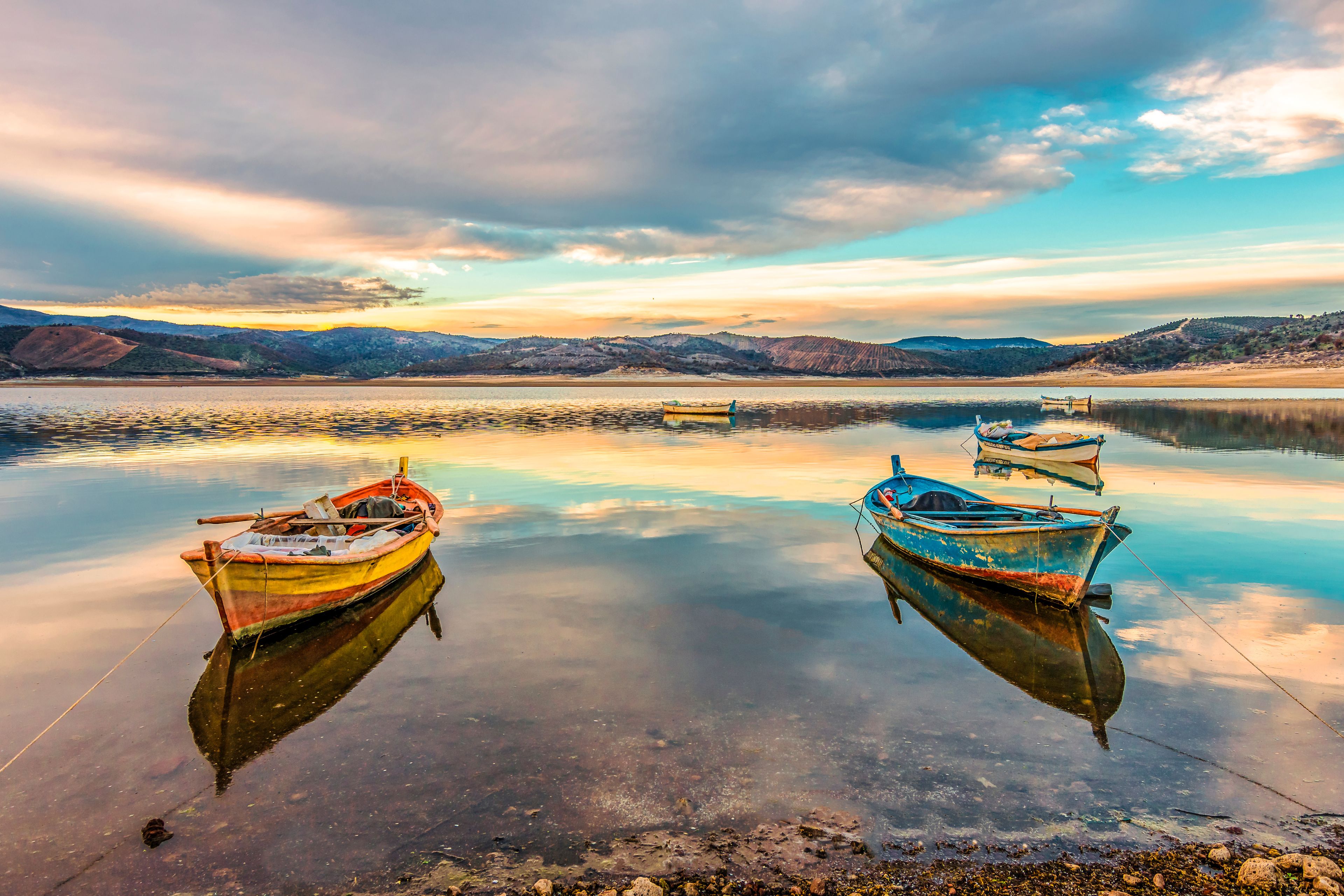 Calm waters with boats anchored, a clear sky, and distant hills.