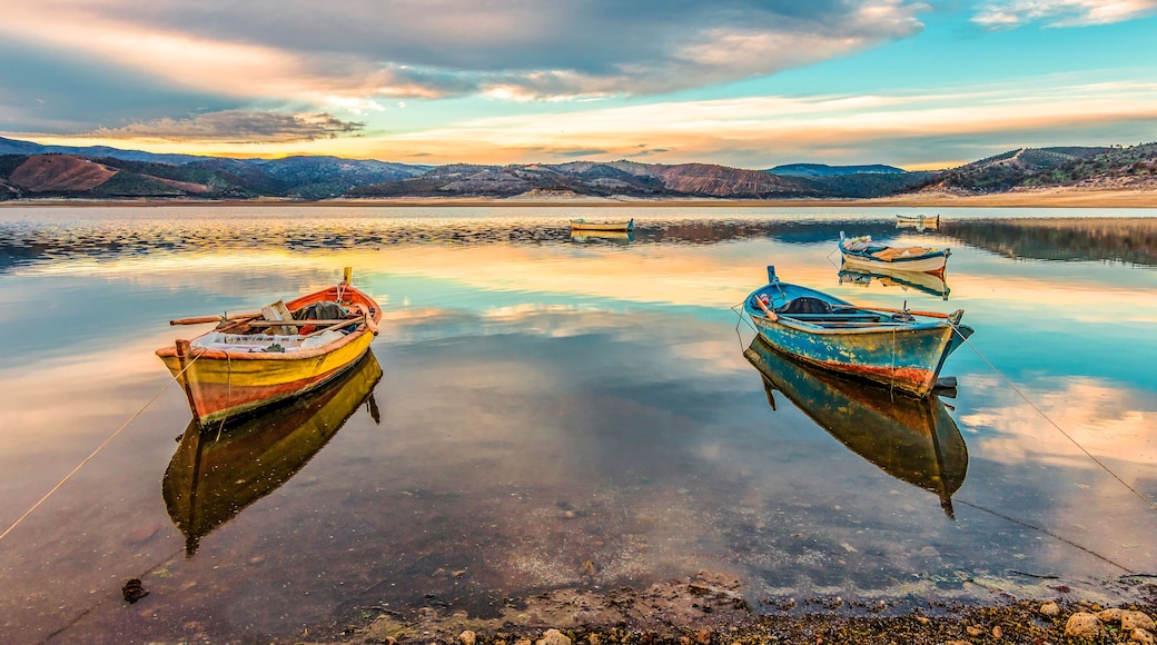 Calm waters with boats anchored, a clear sky, and distant hills.