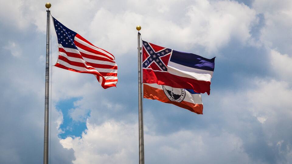 Two flags on flagpoles against a cloudy sky.