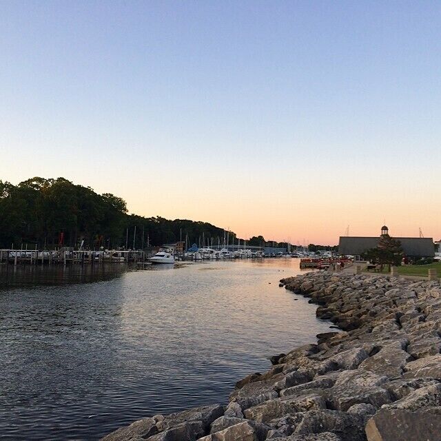 A marina with boats docked, a rocky shoreline, and a building in the background.