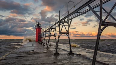 A red lighthouse on a pier with waves crashing against it.