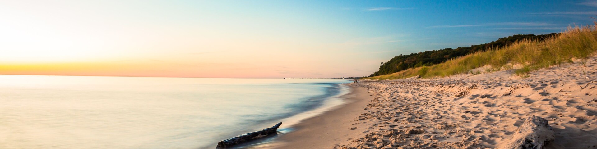 Una playa con un mar tranquilo, una orilla de arena y una duna cubierta de hierba.
