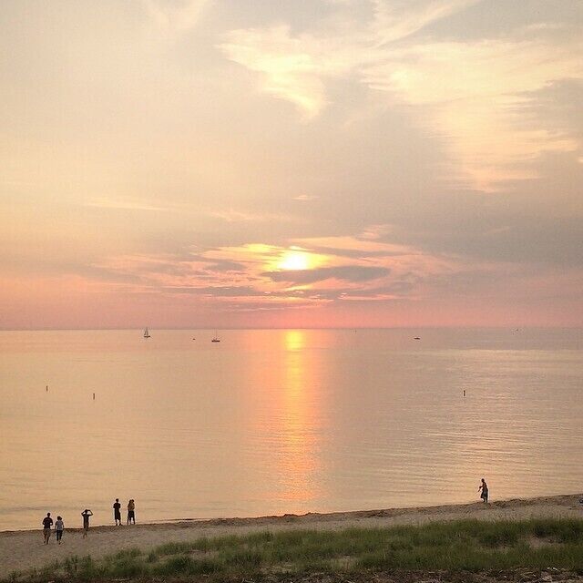 Un atardecer sobre un mar tranquilo con barcos y gente en la orilla.