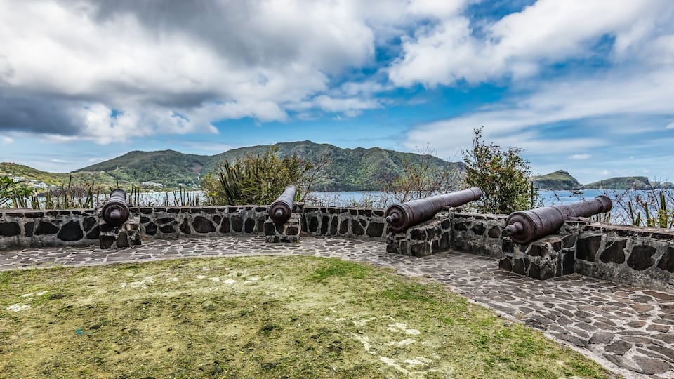 A stone fort with cannons overlooking a body of water and mountains.
