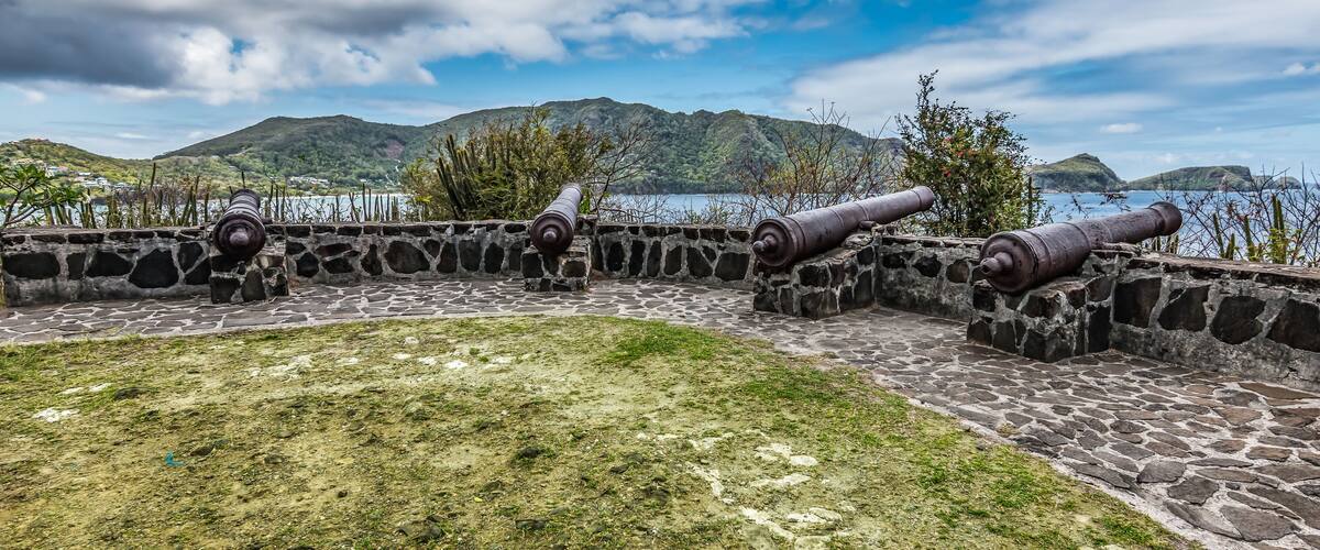 A stone fort with cannons overlooking a body of water and mountains.
