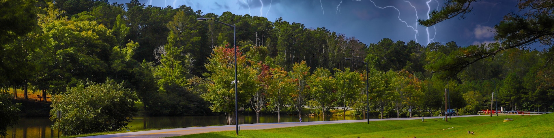 Um parque com gramado, um lago e uma estrada.